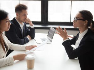 Confident female job applicant talking about experience, expressing thoughts and ideas, HR managers looking suspicious, not liking candidate, doubting, judging. Concept of recruitment stress interview